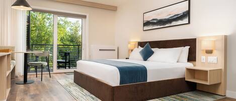 A modern bedroom with a large bed, bedside lamps, a desk, and a view of greenery through the window.