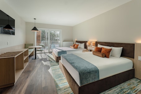 A modern hotel room with a large bed, bedside tables, a desk, and a window with blinds.