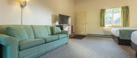 A hotel room with a green sofa, a TV, a bed, and a window with curtains.
