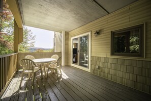 A covered porch with a table and chairs, a sliding glass door, and a window overlooking a natural landscape. - Sun & Ski Inn And Suites (Stowe)