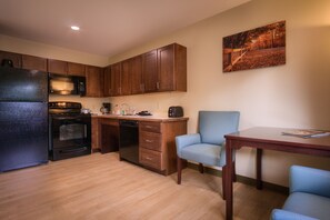 A compact kitchen with wooden cabinets, a refrigerator, an oven, a dishwasher, and a dining area with a table and two chairs. - Sun & Ski Inn And Suites (Stowe)