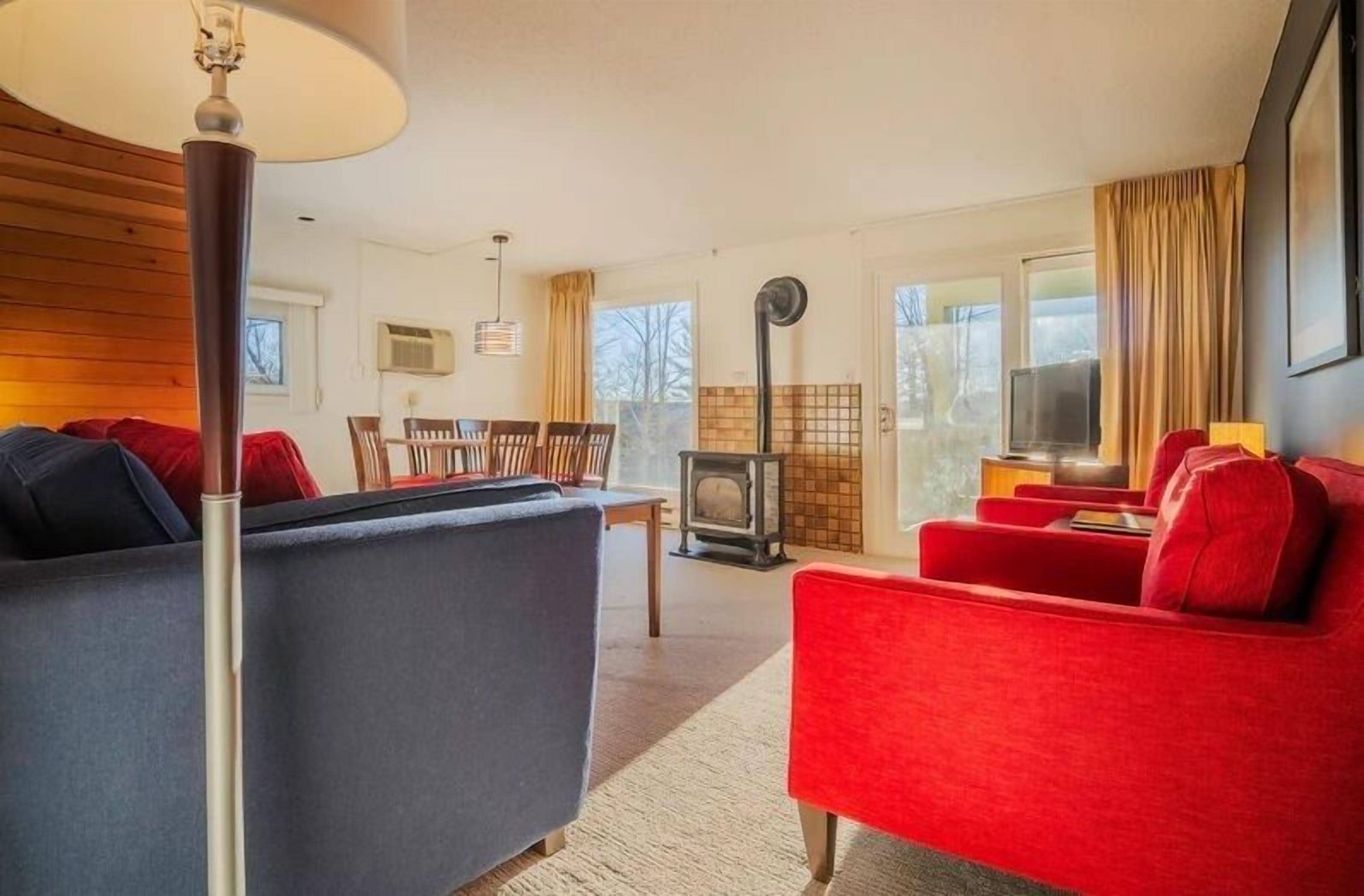 Un salon chaleureux avec un canapé, un fauteuil et un téléviseur. On aperçoit une cheminée au fond.