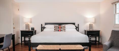 A neatly arranged bedroom with a large bed, bedside tables, a desk, and a chair.