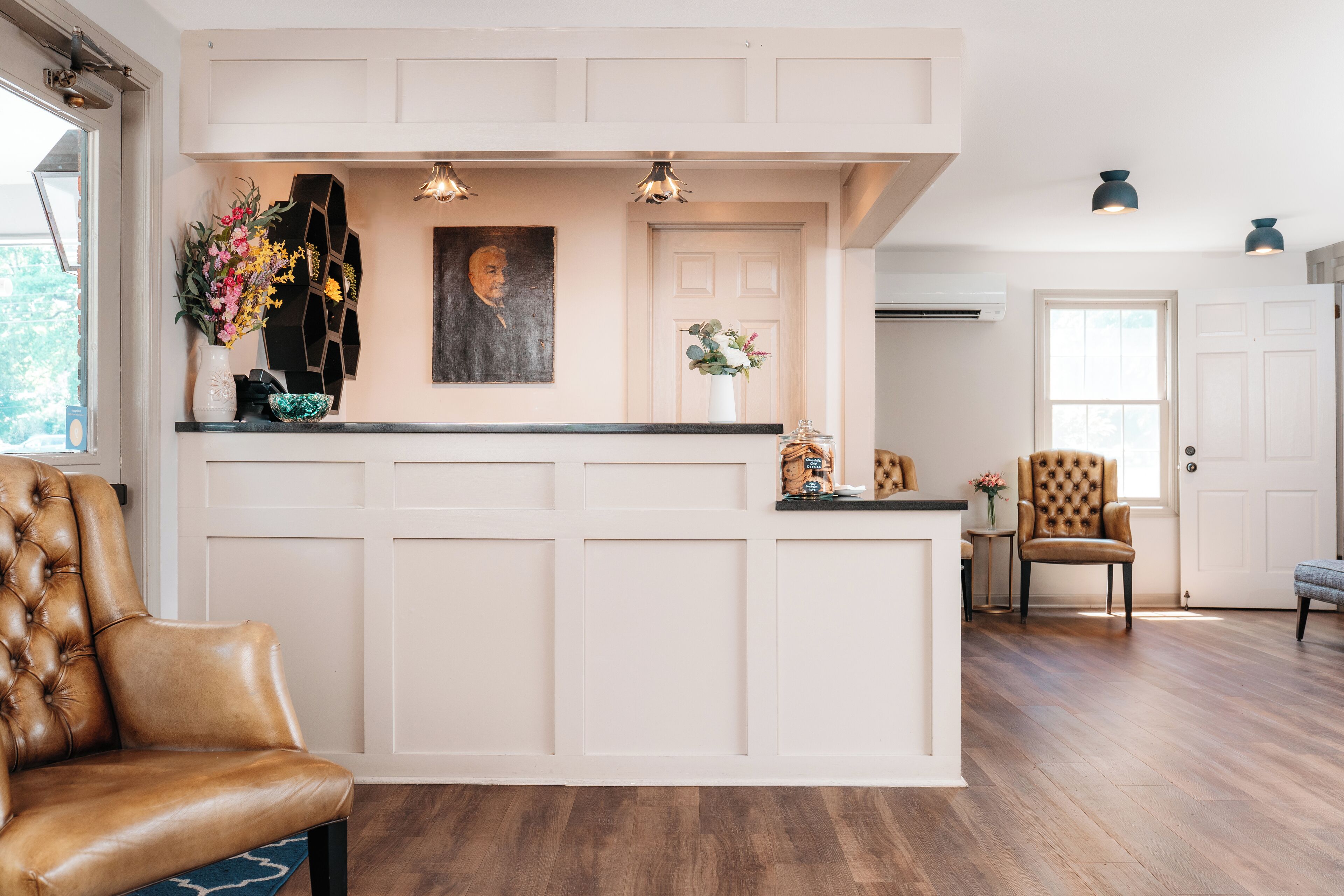 A reception area with a wooden reception desk, a brown leather chair, and a wall-mounted painting.
