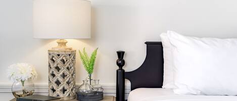 A neatly made bed with white bedding, a black headboard, and a bedside table with a lamp, a book, and decorative items.