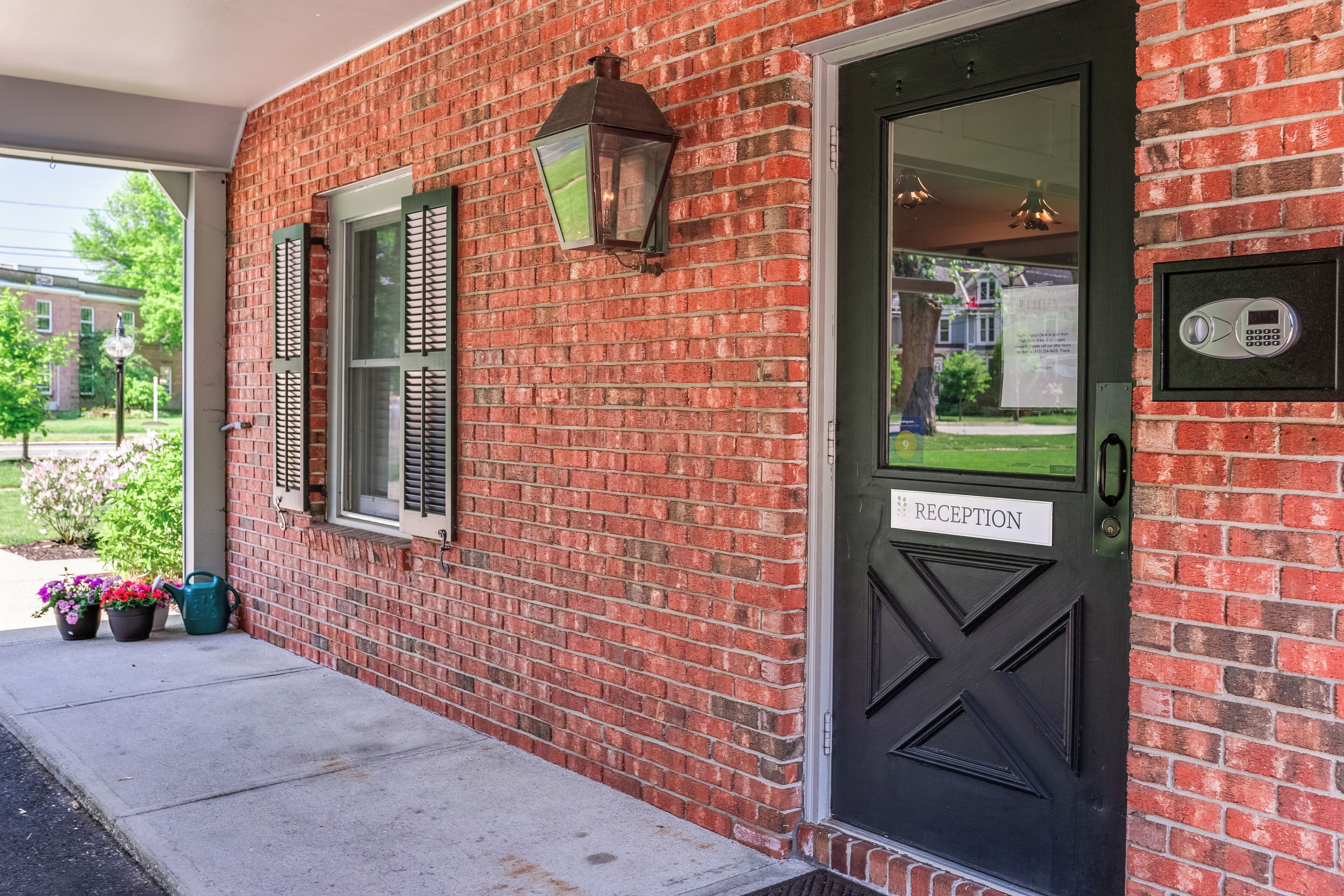 A brick building with a reception door, a mailbox, and a green watering can with flowers.