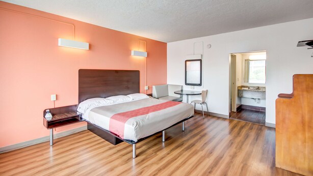 Una habitación de hotel moderna con cama, mesita de noche, silla y un escritorio pequeño con otra silla.