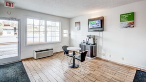 Una habitación de hotel moderna con un ventanal grande, una pequeña mesa redonda con dos sillas, una cafetera y un televisor de pantalla plana montado en la pared.