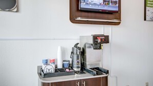 Una estación de café con una cafetera, tazas y un televisor que muestra un noticiero.