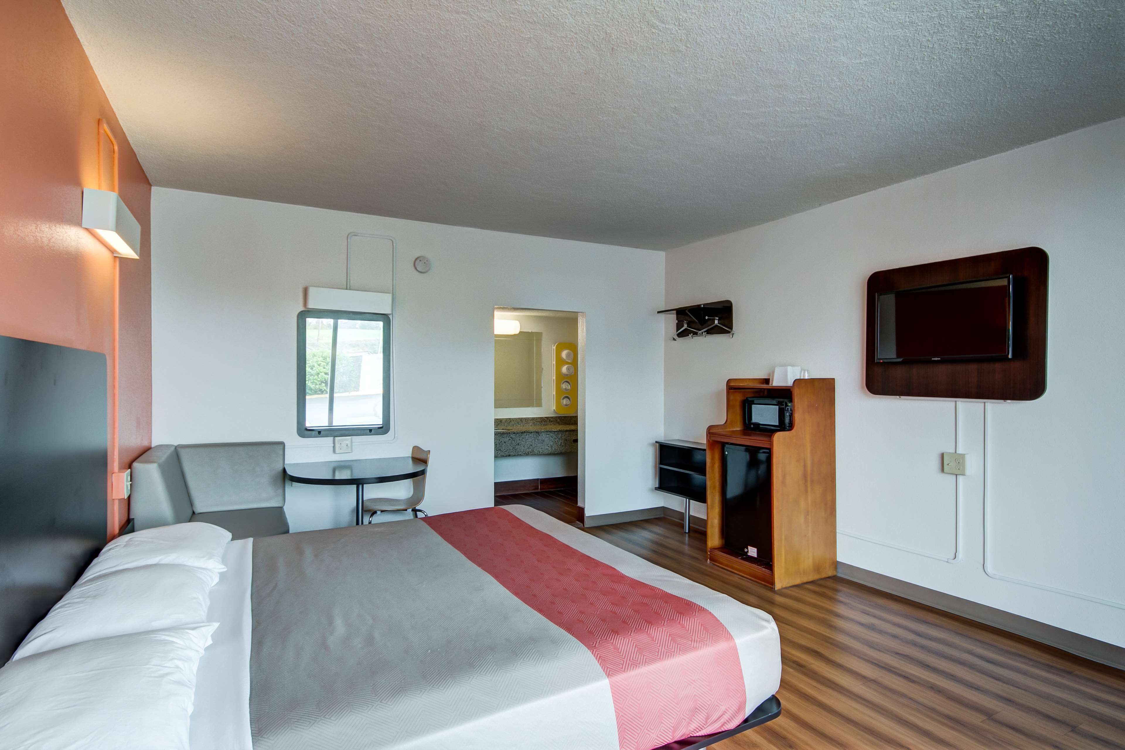 A hotel room with a bed, a desk, a chair, a TV, and a small kitchenette.