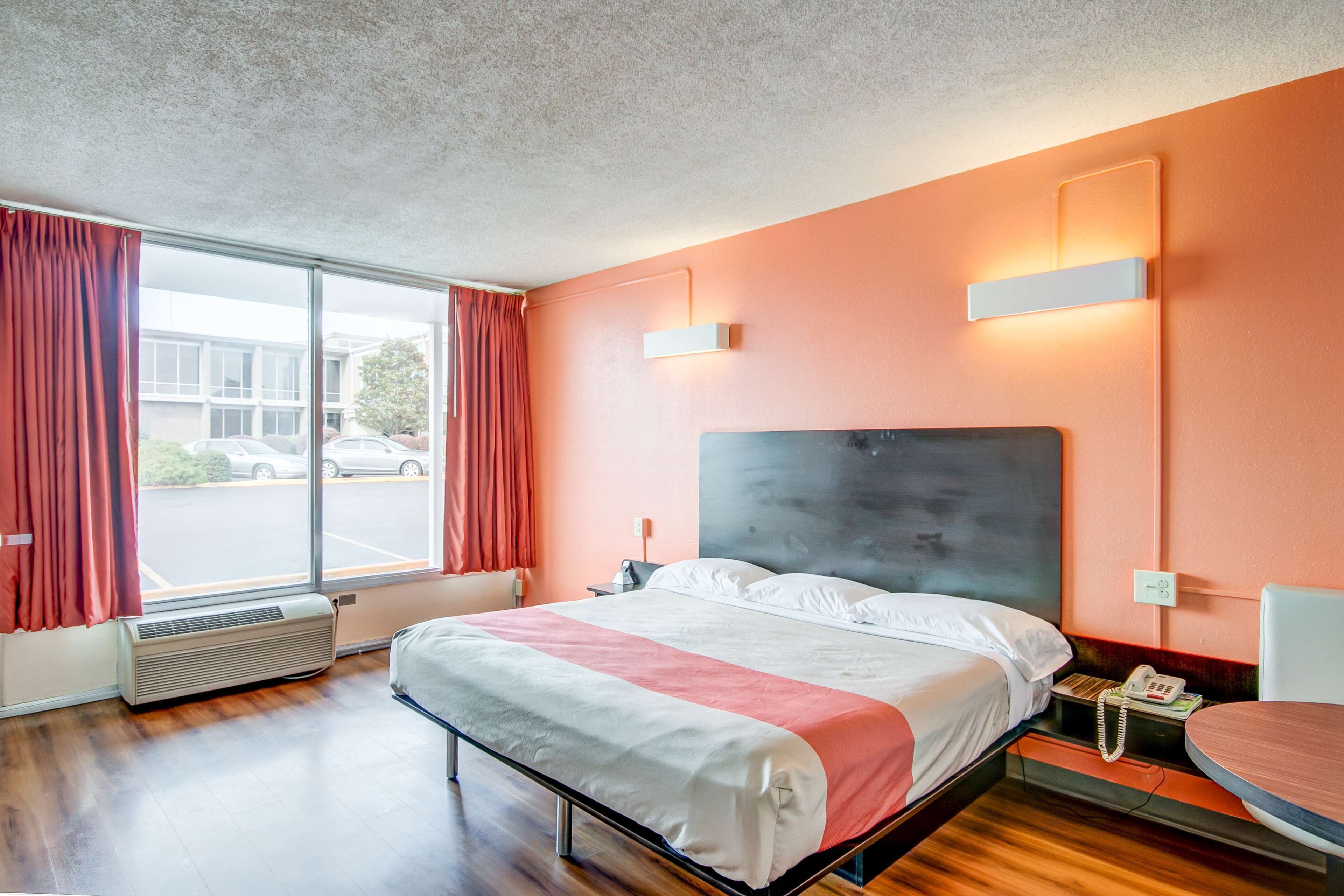 Une chambre d’hôtel avec un grand lit, une table de chevet avec un téléphone, une fenêtre avec des rideaux et un luminaire fixé au mur.