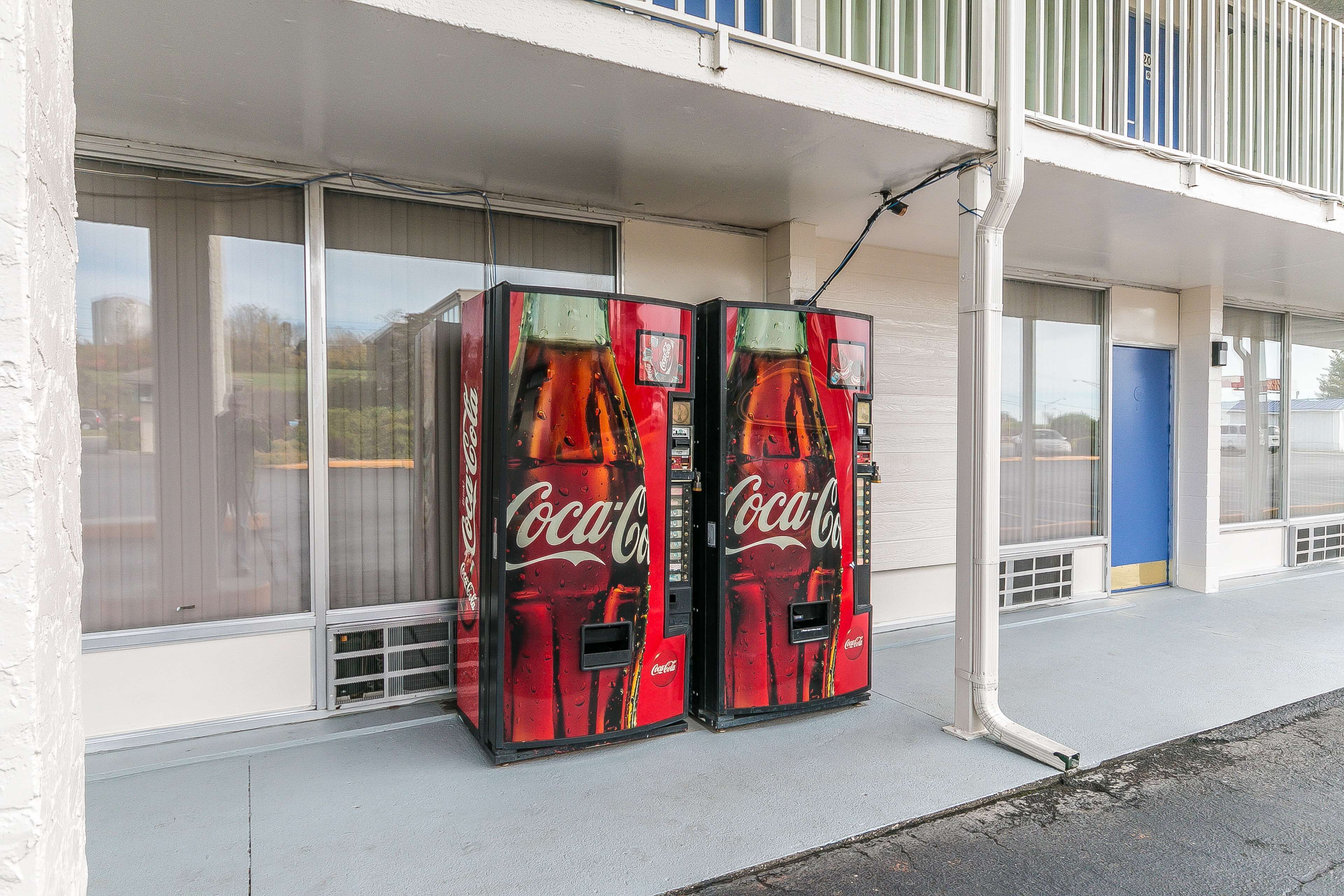 Two Coca-Cola vending machines outside a building with large windows and a blue door.