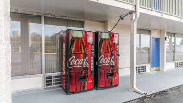 Two Coca-Cola vending machines outside a building with large windows and a blue door.