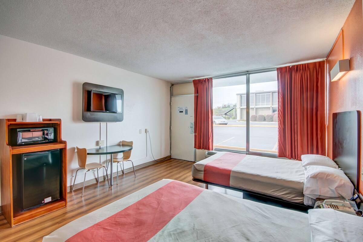 A hotel room with two beds, a desk, a chair, a television, and a window with curtains.