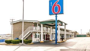Un motel con un llamativo letrero con el número '6', un área cubierta al aire libre y una escalera que lleva a la entrada.