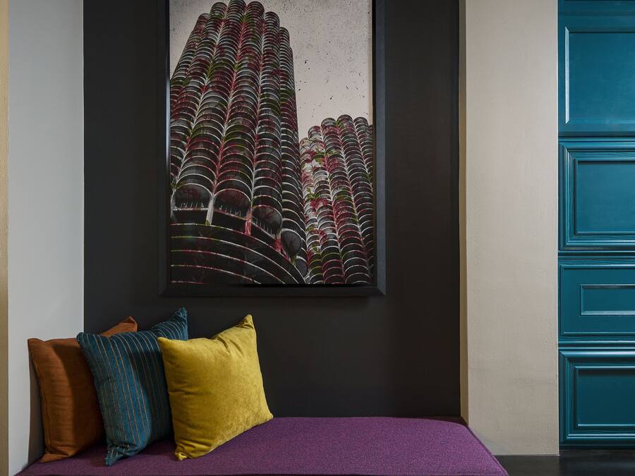 Una habitación moderna con pared oscura, una obra de arte enmarcada, un sofá púrpura con cojines y un mueble azul.