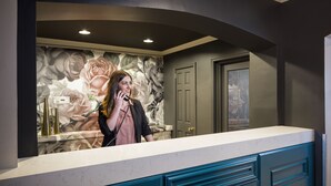 A reception area with a counter, a floral wall mural, and a door in the background.