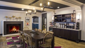 A dining area with a fireplace, a wooden table, and chairs. There is a kitchen area with cabinets and appliances.