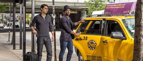 A taxi with a yellow cab sign and a phone number on the side, parked on a city street.