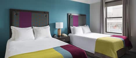 A hotel room with two beds, a ceiling fan, a window with curtains, and a view of the city.