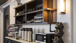 A kitchen with a microwave, coffee makers, and a shelf with glassware and dishes.