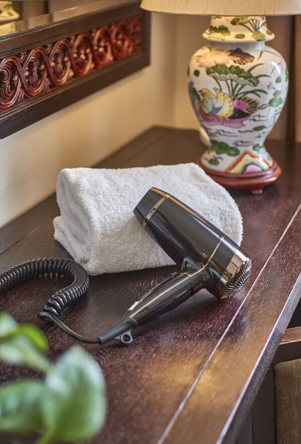 A hair dryer on a wooden surface with a towel and a decorative lamp in the background. - Village Hotel Albert Court by Far East Hospitality (Singapore)
