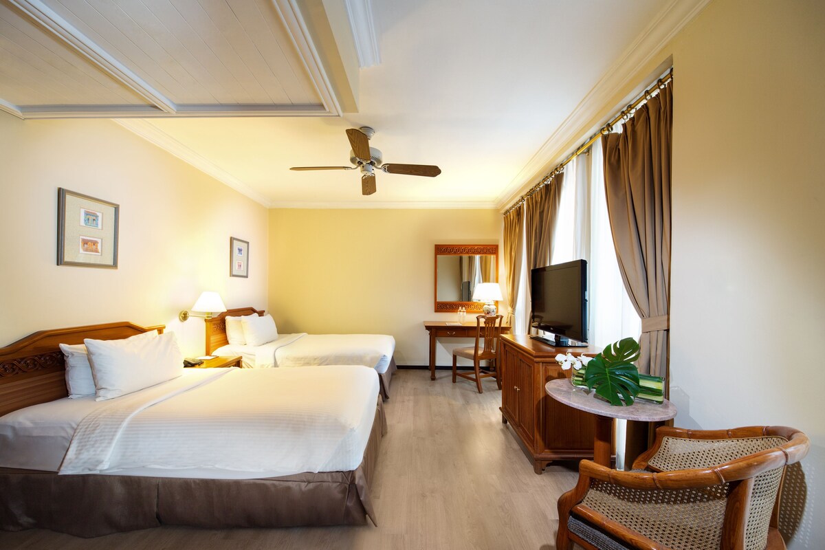 Une chambre d’hôtel avec deux lits, un bureau, une télévision et un ventilateur de plafond.