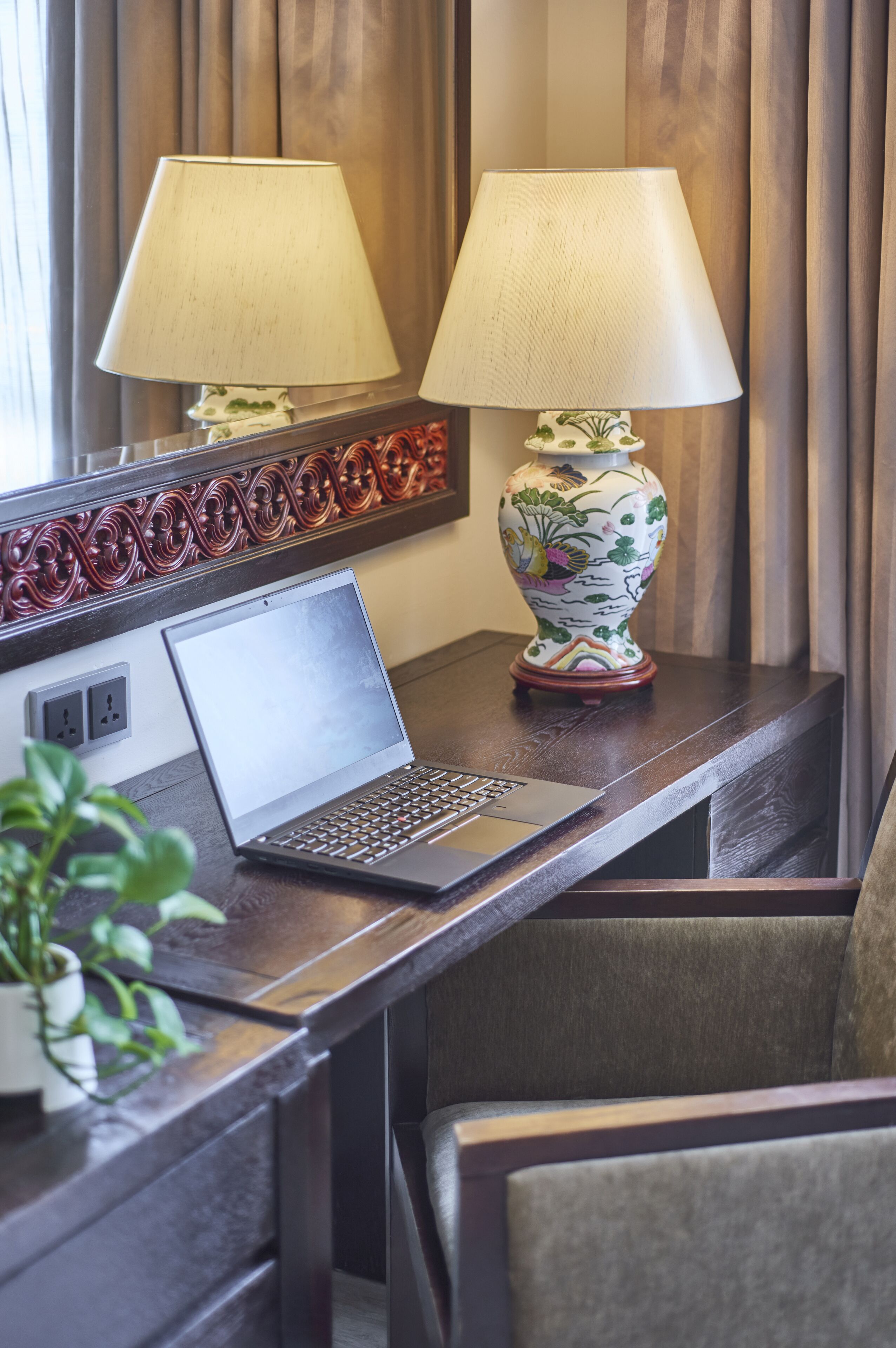 A hotel desk with a laptop, two lamps, and a decorative vase.