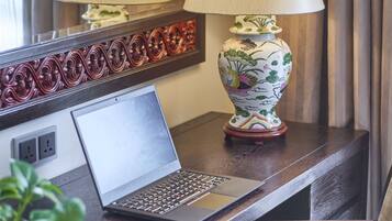 A hotel desk with a laptop, two lamps, and a decorative vase.