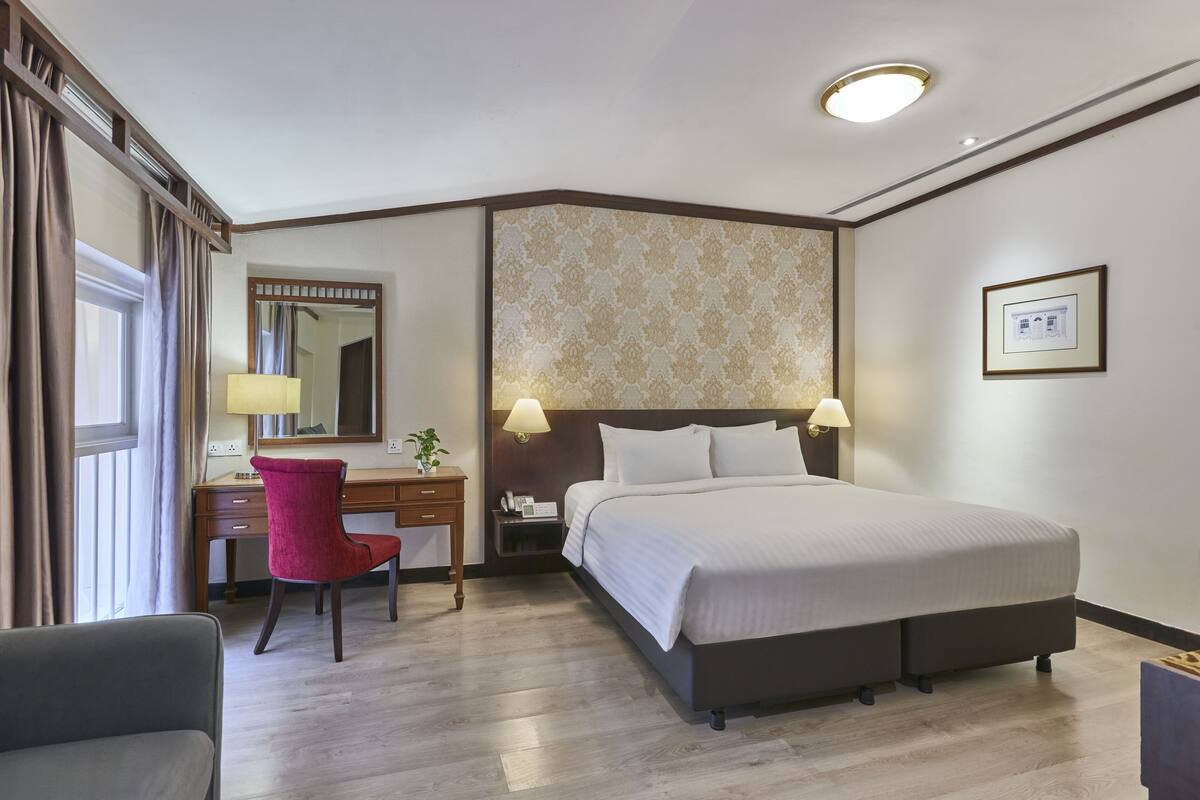A hotel room with a large bed, a desk with a chair, a mirror, and a nightstand with a lamp.