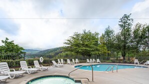 A swimming pool area with lounge chairs and a hot tub, surrounded by trees and a view of hills. - Gatlinburg Chateau Rentals (Gatlinburg)