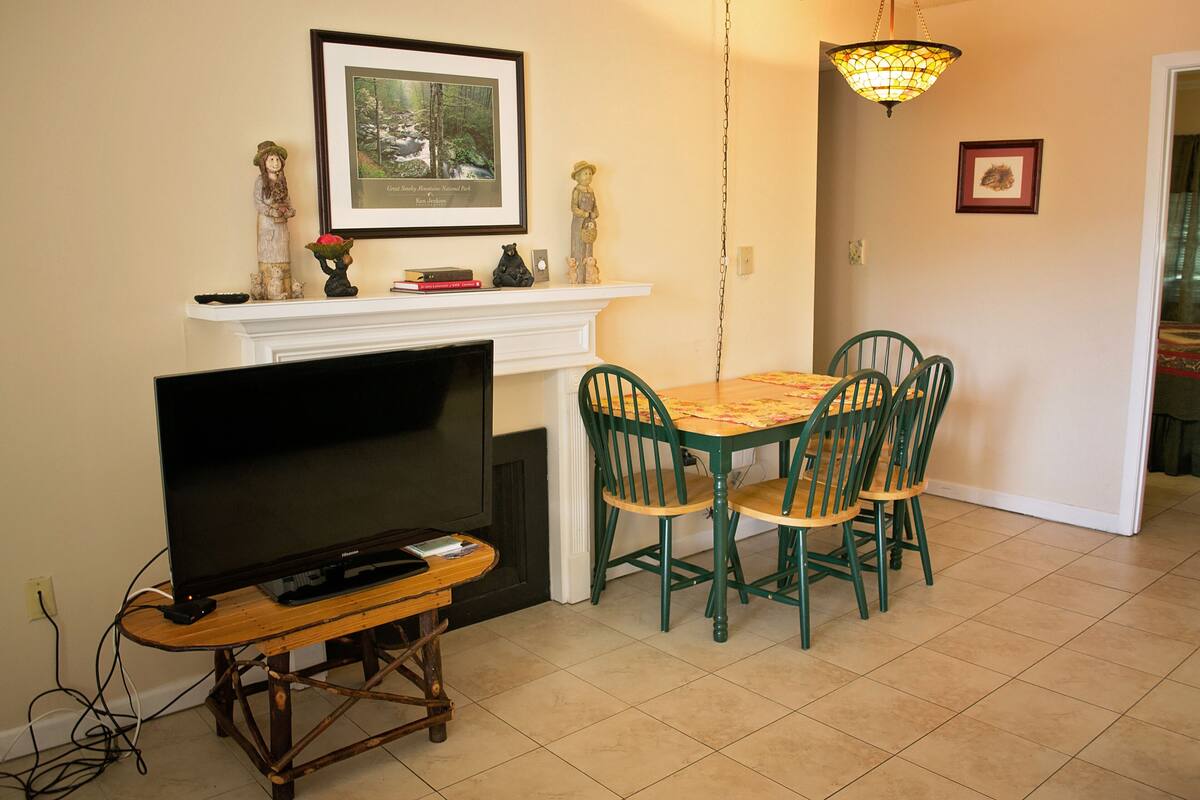 A dining area with a table and chairs, a fireplace, a television on a stand, and a framed picture on the wall.