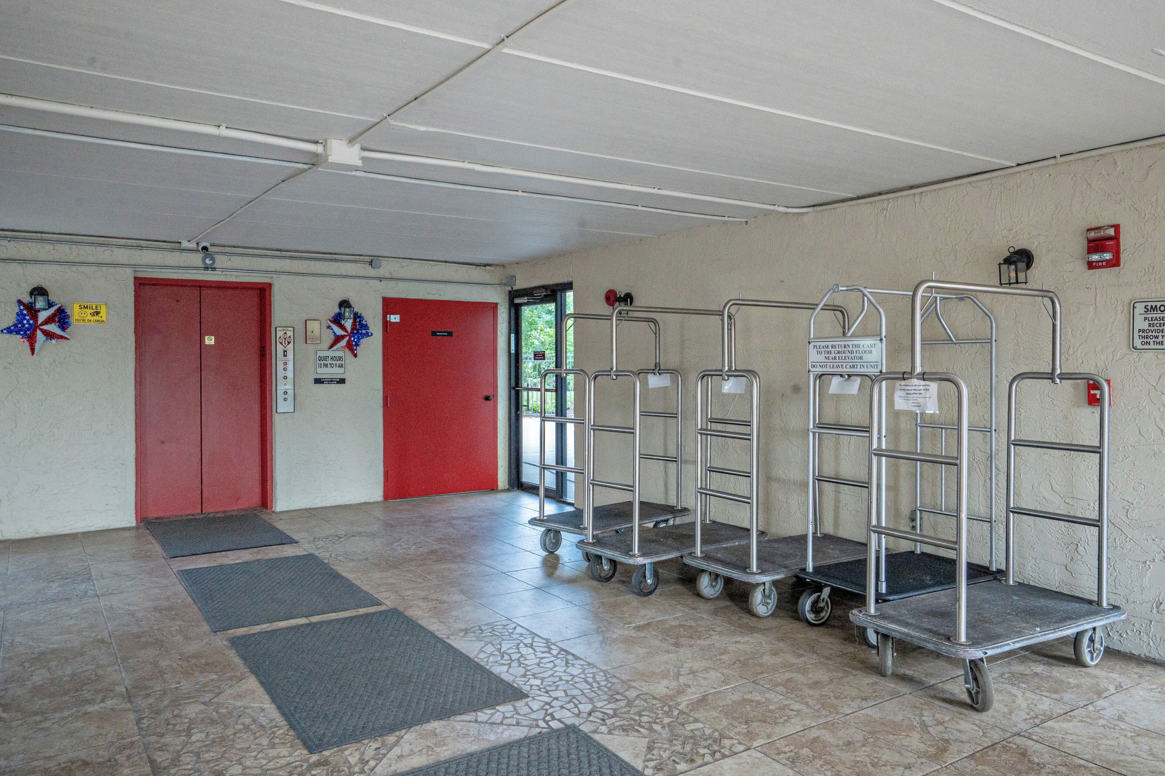 Een hotelhal met een rode lift, een brandmelder en een bordje met daarop de stilte-uren vermeld.