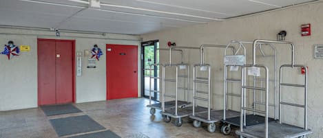 Een hotelhal met een rode lift, een brandmelder en een bordje met daarop de stilte-uren vermeld.