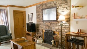 A cozy living room with a stone fireplace, a television, a wooden coffee table, and a dining area with bar stools. - Gatlinburg Chateau Rentals (Gatlinburg)