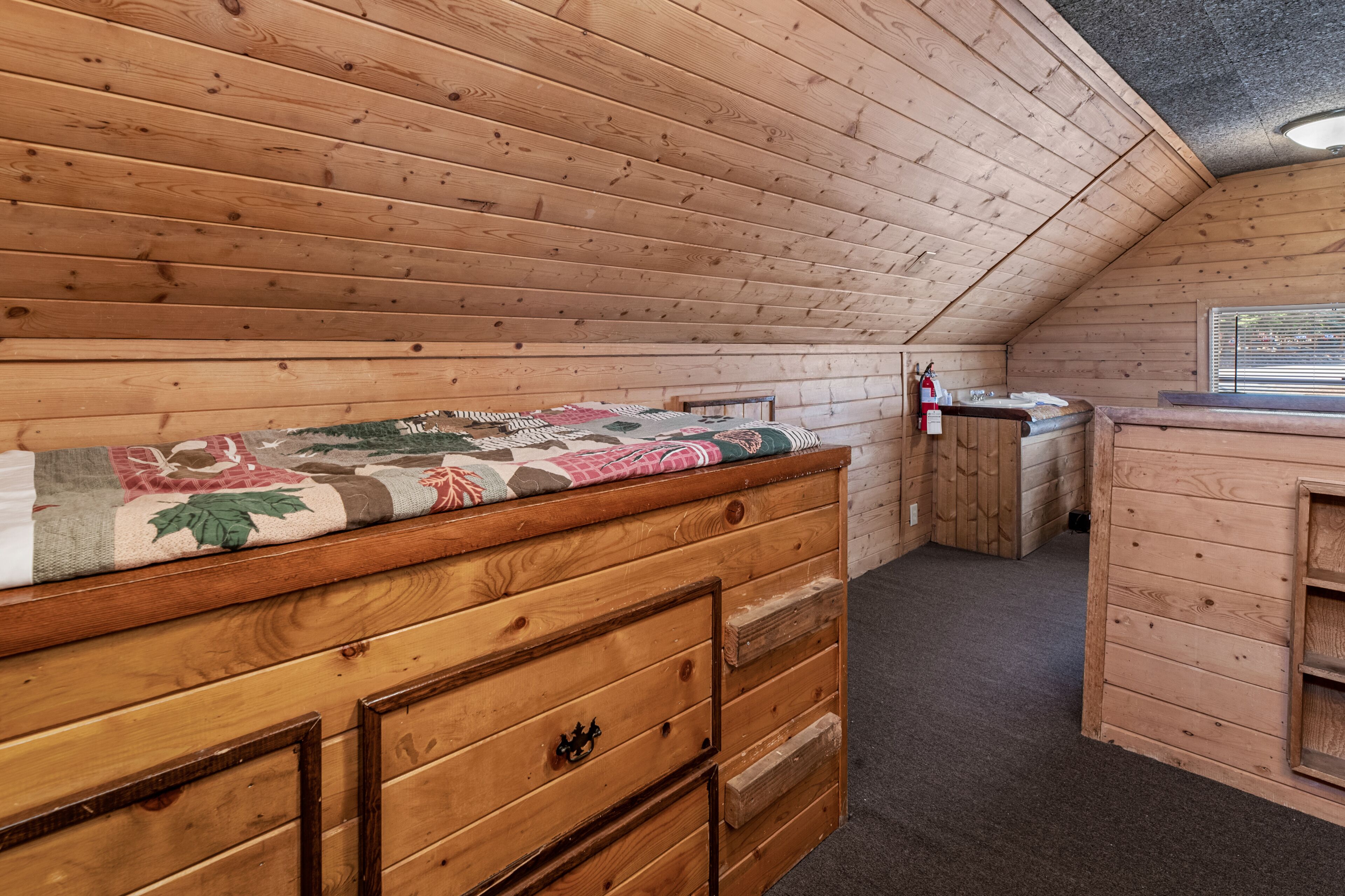 A cozy attic bedroom with a wooden bunk bed, a small desk, and a window.