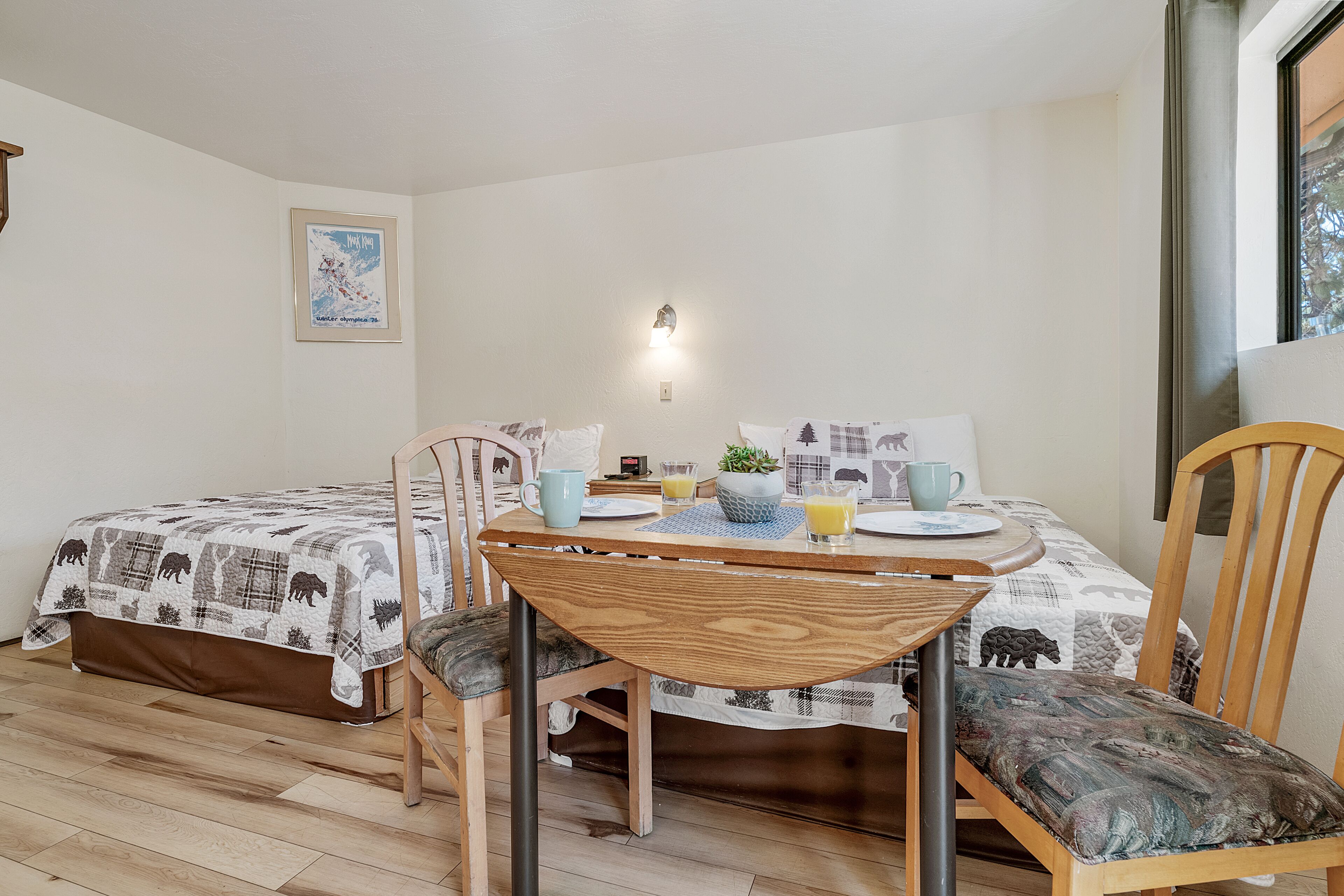 A room with a bed, a table with chairs, a wall-mounted light, and a framed picture.