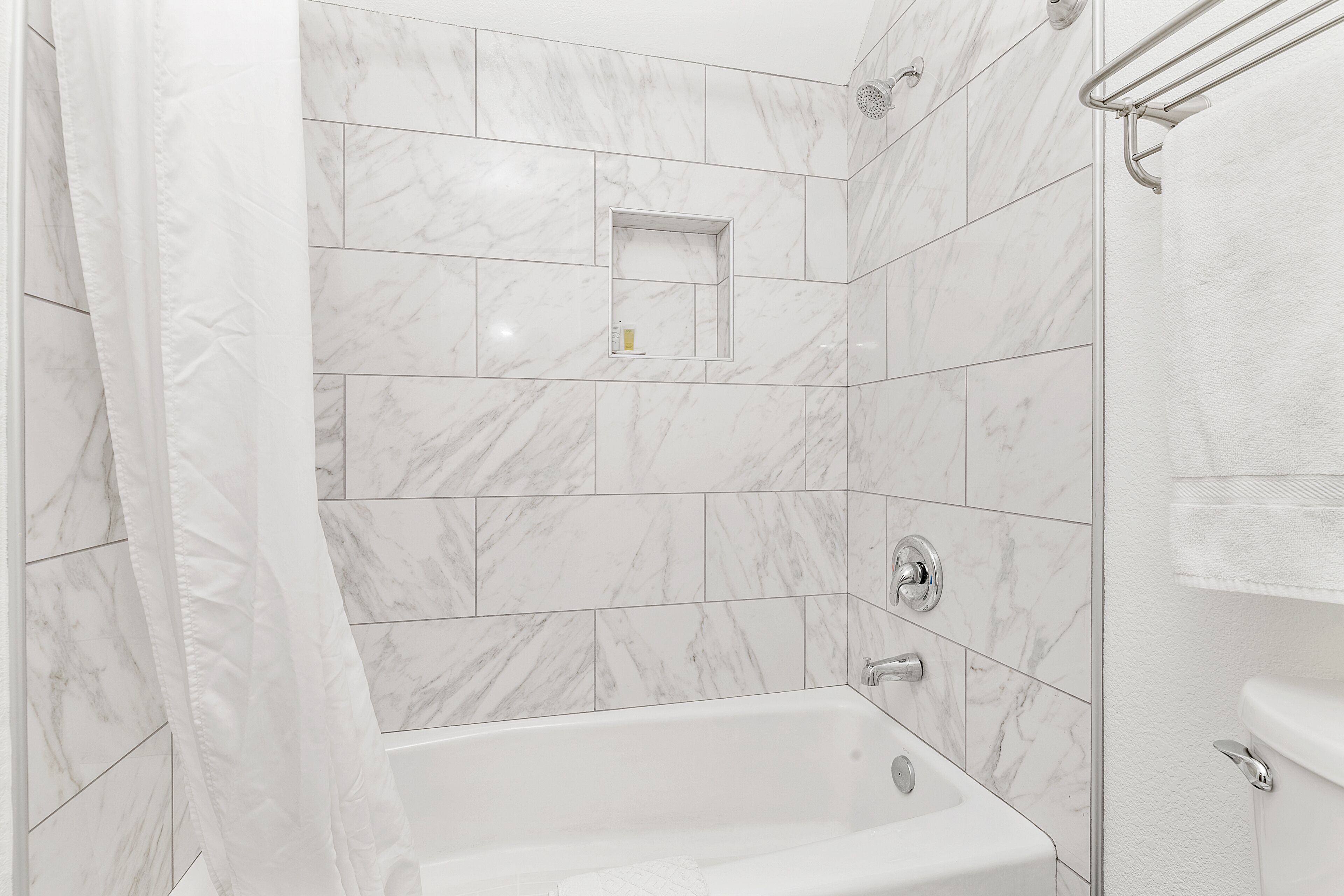 Un baño moderno con bañera, azulejos de mármol blanco y zona de ducha.