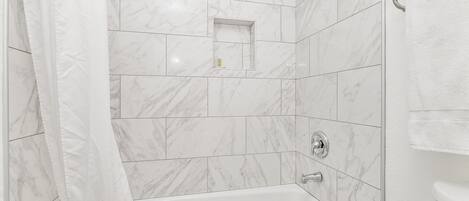Une salle de bain moderne avec une baignoire, des carreaux de marbre blanc et un espace douche.