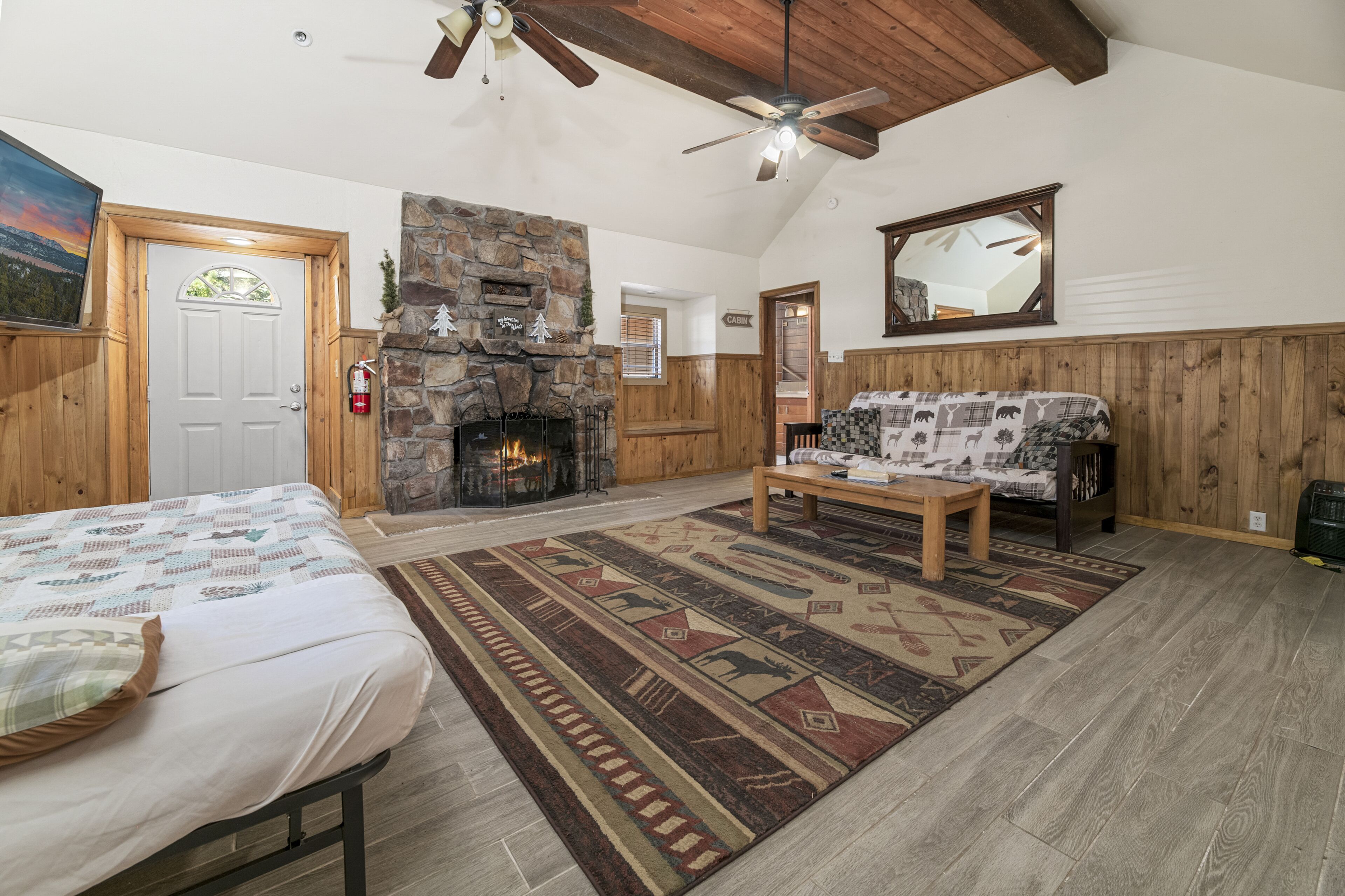 A spacious room with a stone fireplace, wooden walls, a ceiling fan, and a large bed.