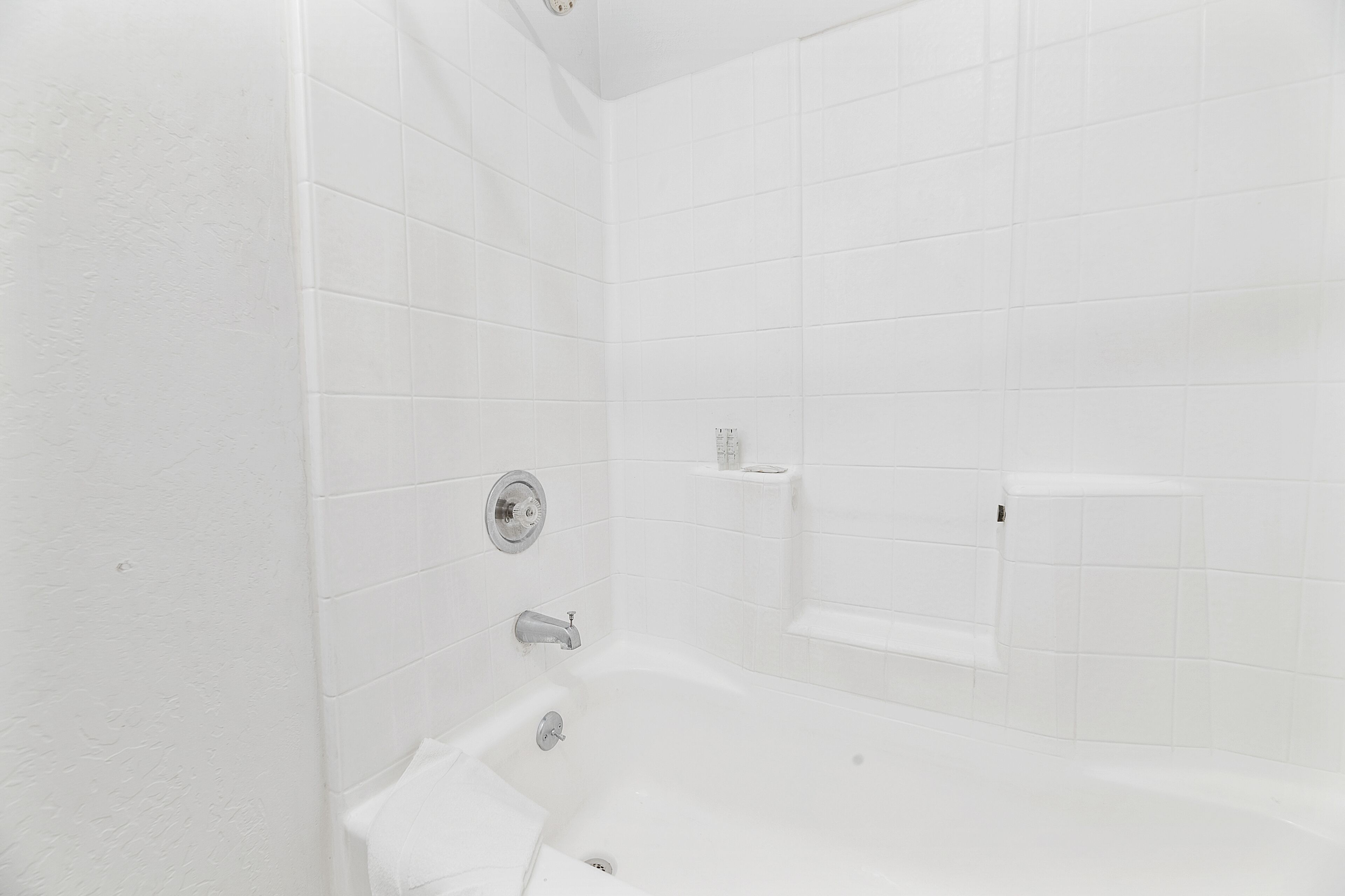 Une salle de bain aux murs recouverts de carreaux blancs, équipée d’une baignoire, de toilettes et d’un espace douche.