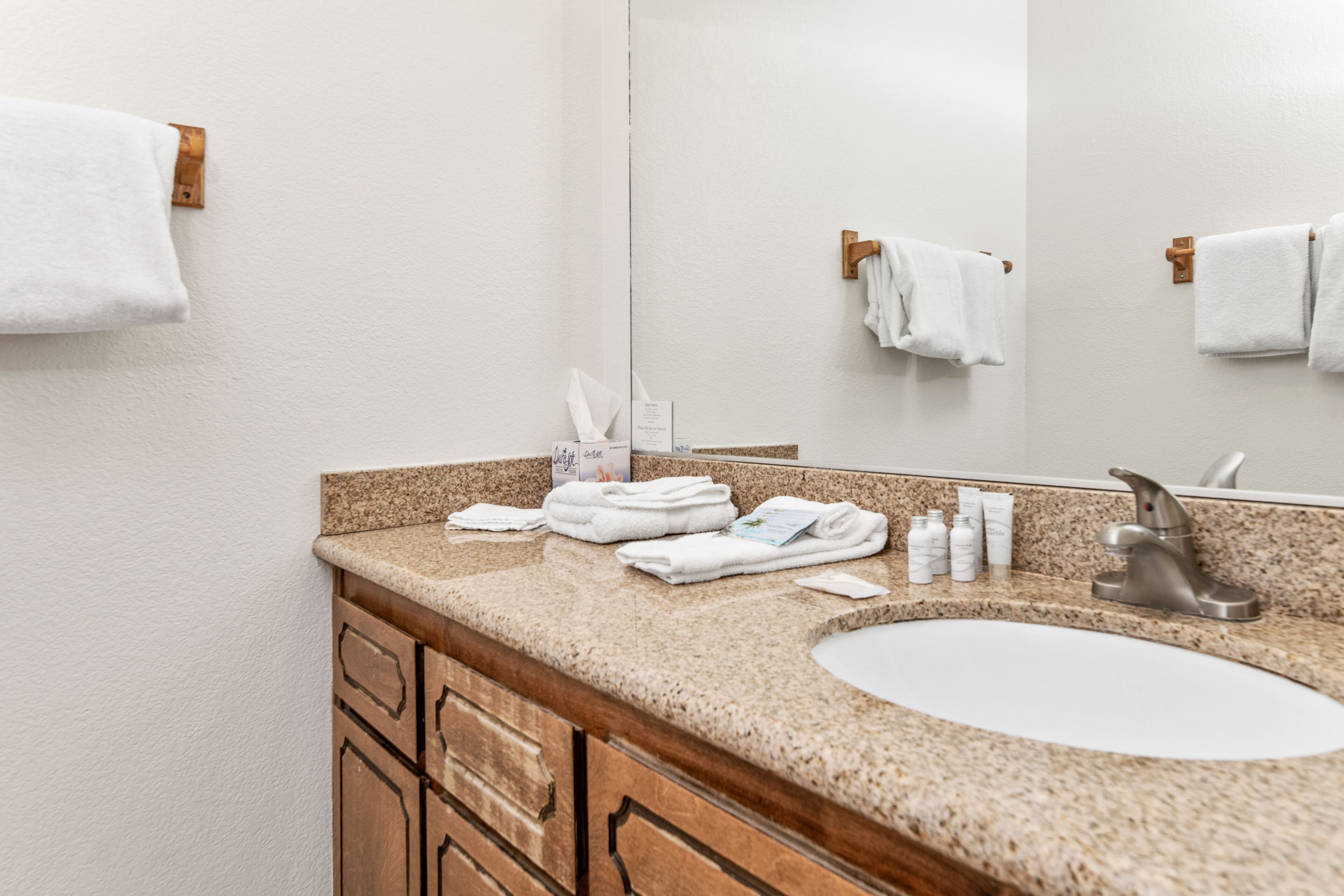 A bathroom with a granite countertop, a white sink, and wooden cabinets. There are towels and toiletries on the counter.