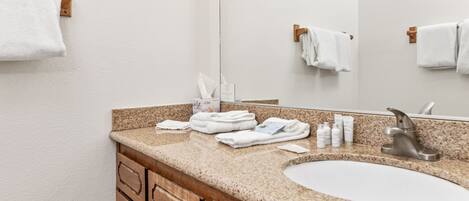 A bathroom with a granite countertop, a white sink, and wooden cabinets. There are towels and toiletries on the counter.