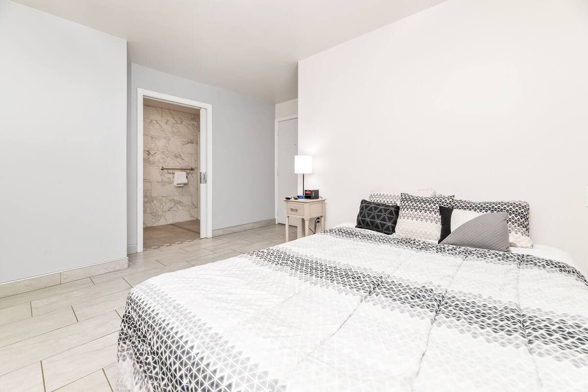 Ein Schlafzimmer mit einem großen Bett, einem Nachttisch mit Lampe und einer Tür zu einem Badezimmer.