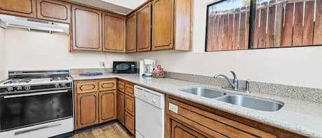 A kitchen with wooden cabinets, a stove, a dishwasher, a microwave, and a sink.