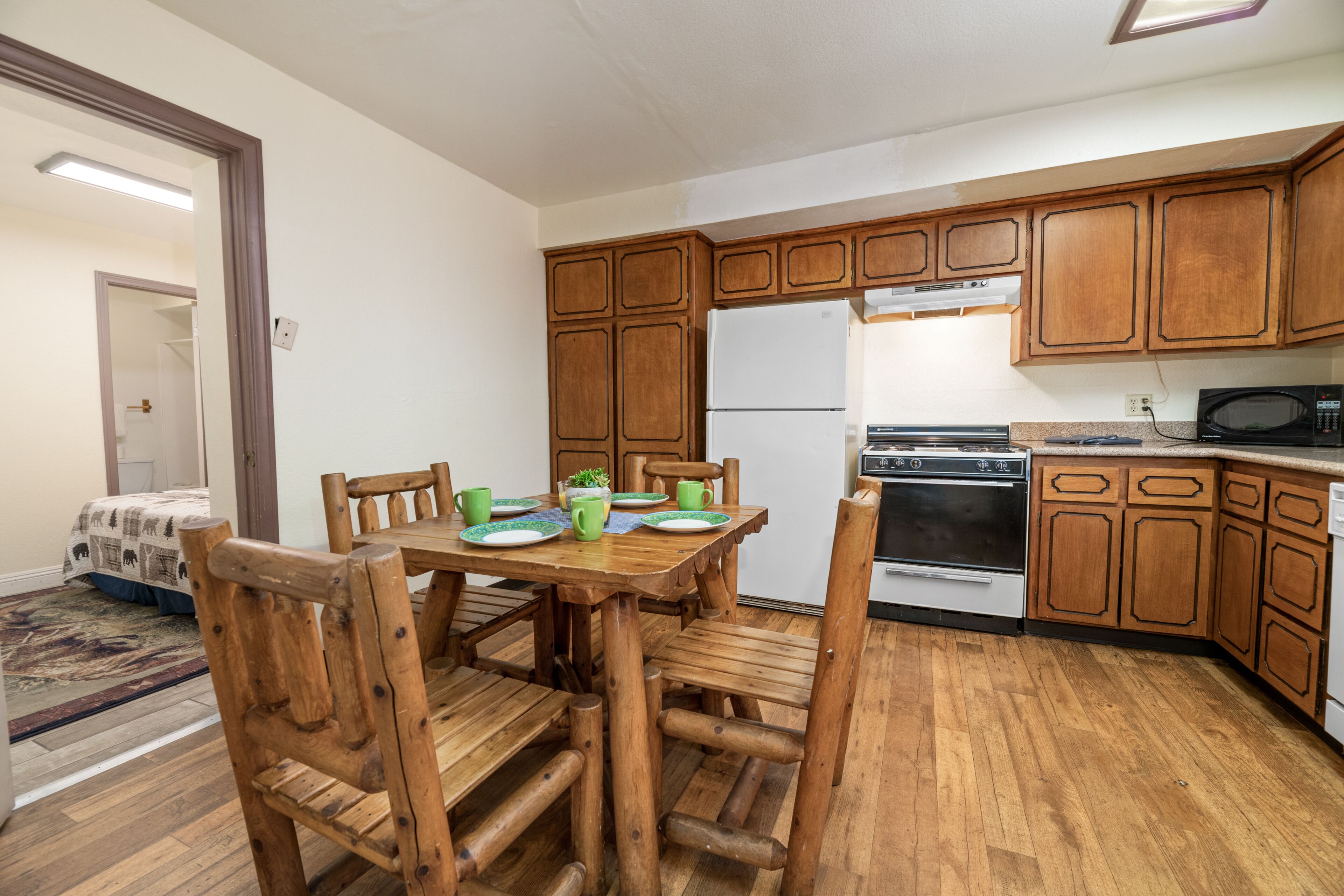 Una cocina con armarios de madera, refrigerador, estufa, microondas y una mesa de comedor con sillas.