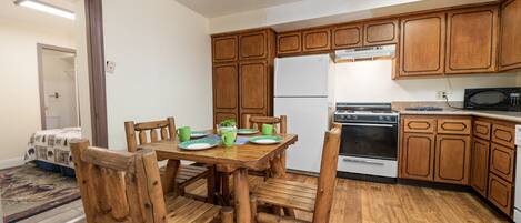 Una cocina con armarios de madera, refrigerador, estufa, microondas y una mesa de comedor con sillas.