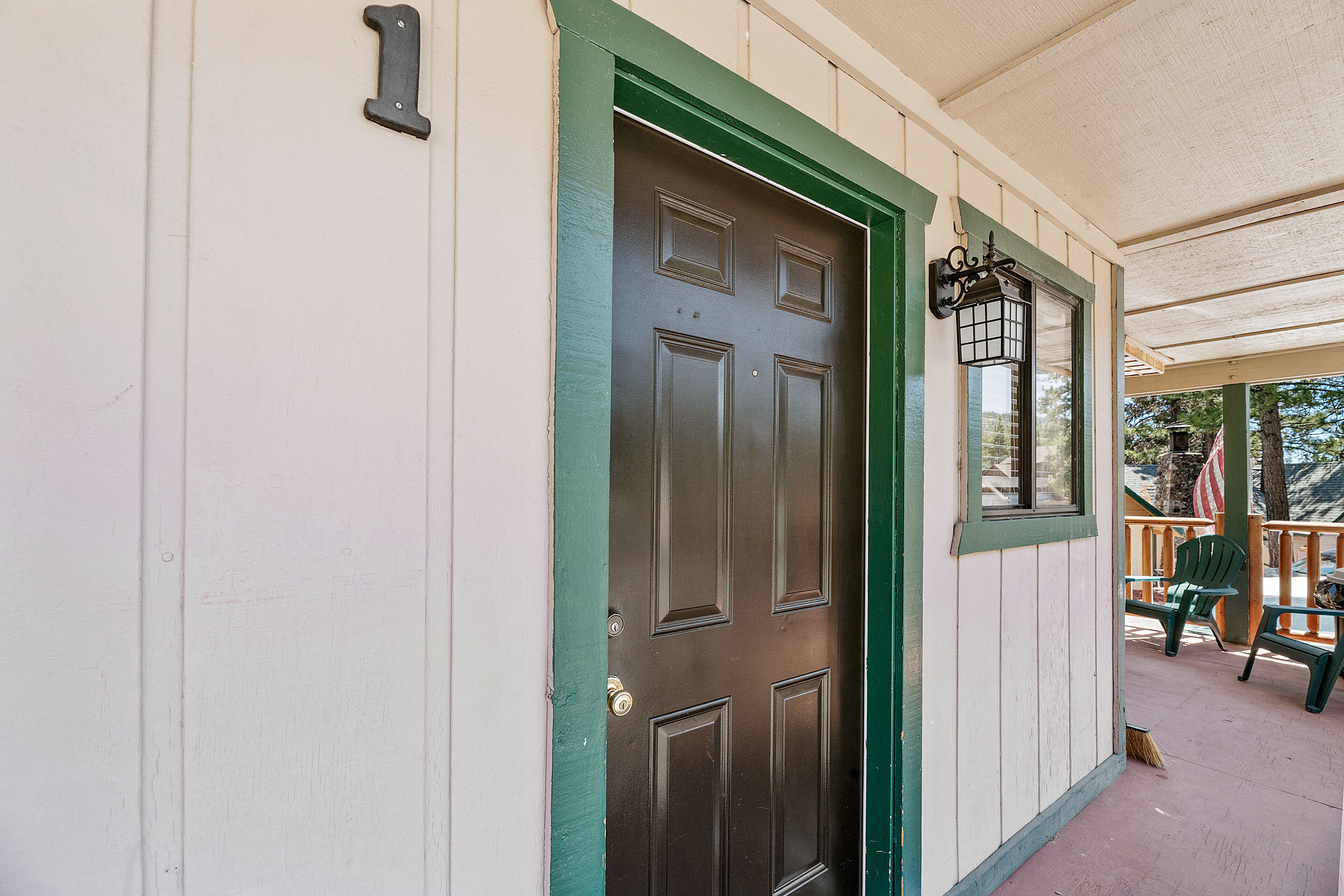 Un edificio blanco con puerta verde y un porche con sillas y una mesa.
