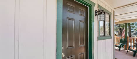 Un edificio blanco con puerta verde y un porche con sillas y una mesa.