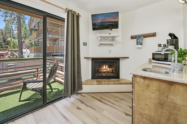 A modern kitchen with a fireplace, a flat-screen TV, and a dining area with a bench and table. - Big Bear Lakefront Lodge (Big Bear Lake)